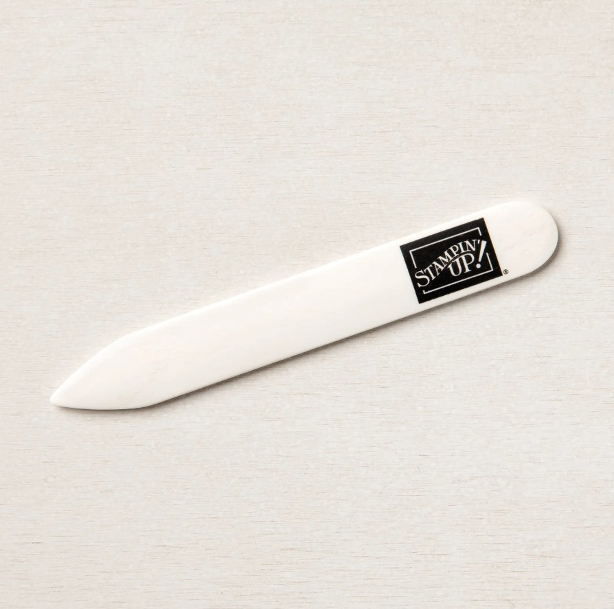 Stampin’ Up! bone folder tool with a smooth ivory finish, resting on a light wooden surface.