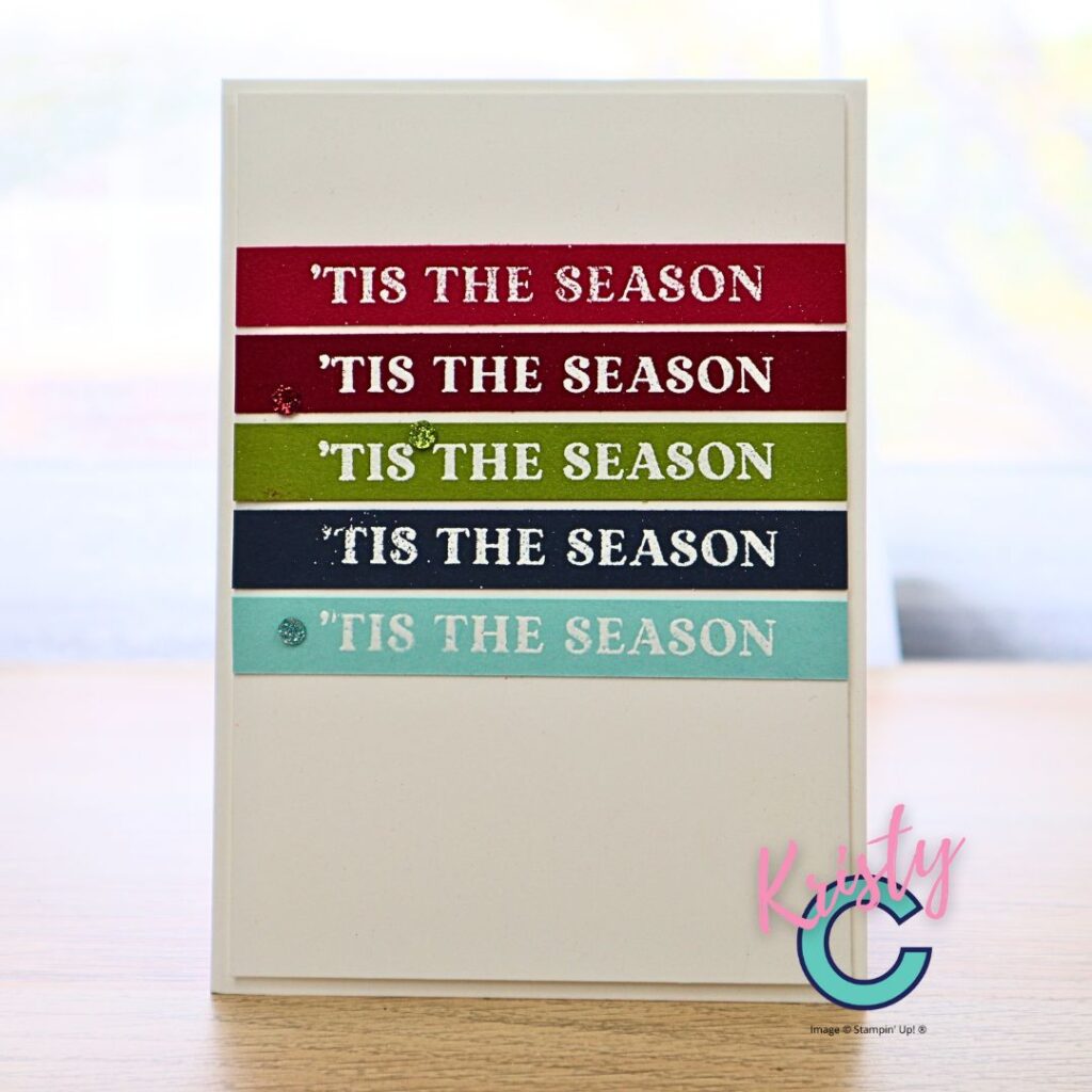 Clean and simple handmade card with horizontal colour-blocked strips in red, green, navy, and aqua, each heat-embossed with “’Tis the Season.”