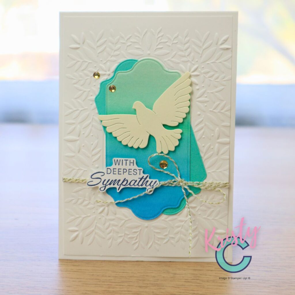 A handmade sympathy card featuring a white dry-embossed leafy background, a soft teal and aqua layered label, and a cream dove die cut with a “With Deepest Sympathy” sentiment, designed by Kristy Coromandel using Stampin’ Up! products.