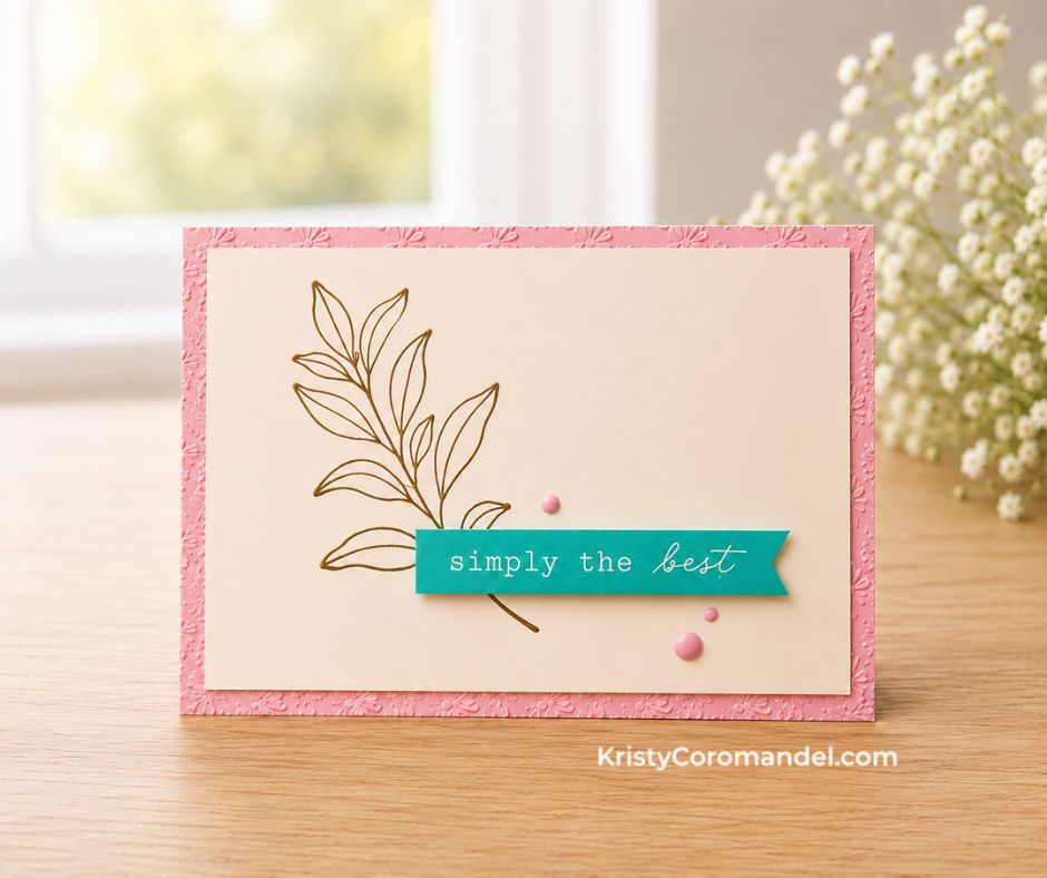 A handmade card featuring a soft pink embossed border, minimalist botanical line-art stamp, teal "Simply the Best" sentiment banner and pink enamel dots, photographed on a warm timber surface with a softly blurred window and baby's breath in the background.