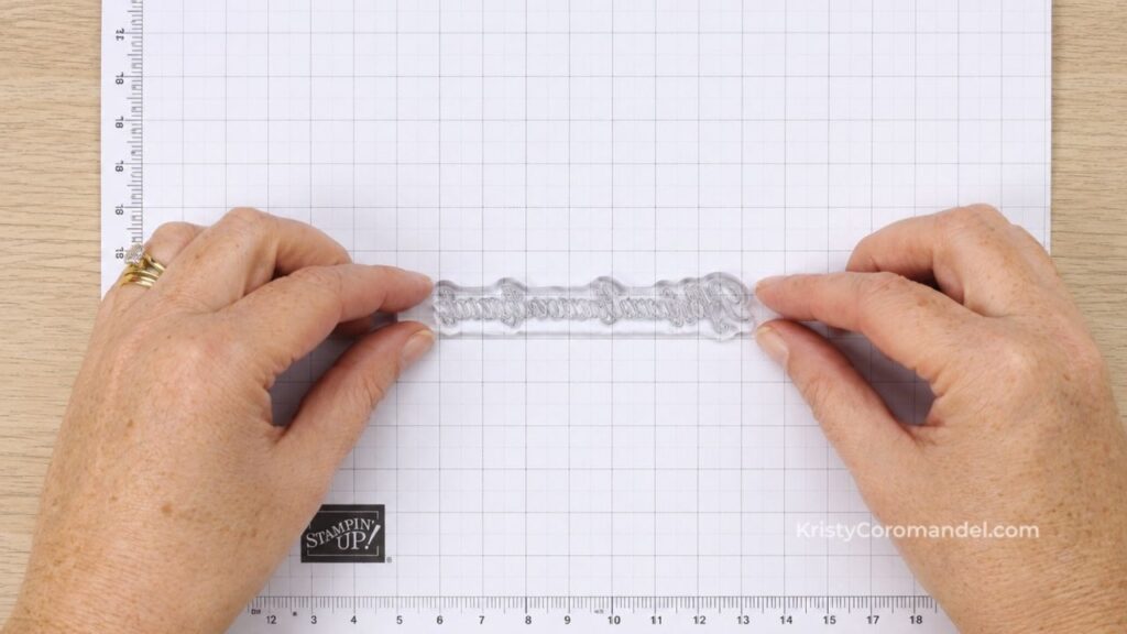 Overhead view of a clear sentiment stamp positioned face-down on grid paper and aligned with the grid lines to ensure straight stamping on handmade cards.