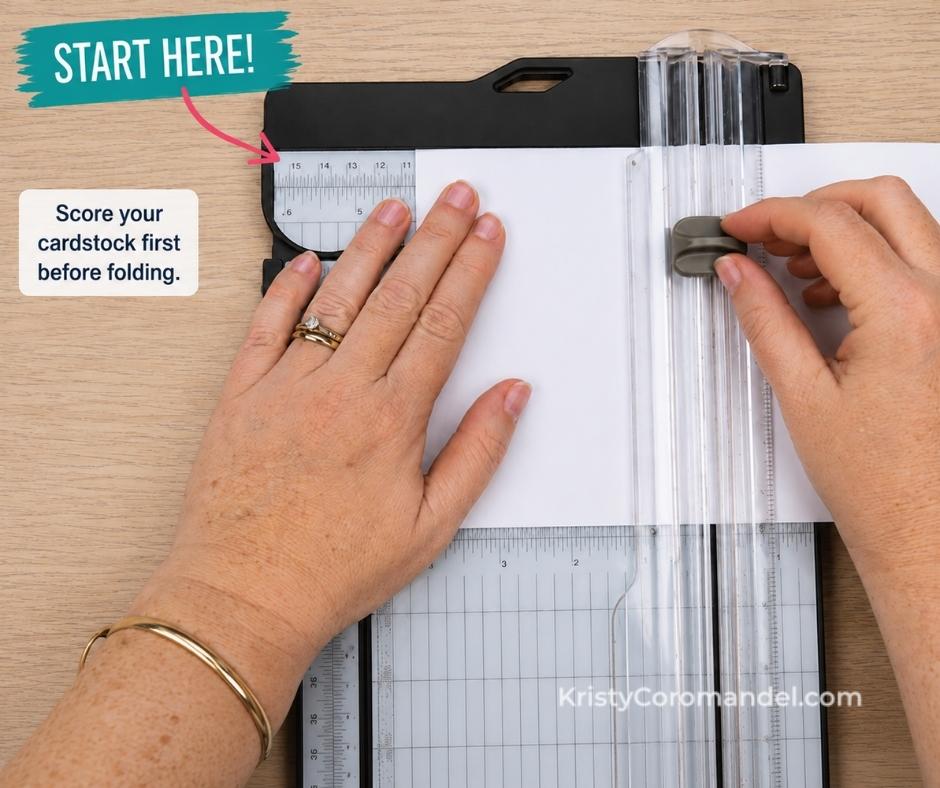 Close-up overhead view of cardstock being scored on a paper trimmer before folding, with hands positioning the scoring blade and a reminder to score cardstock first for crisp, professional card folds.