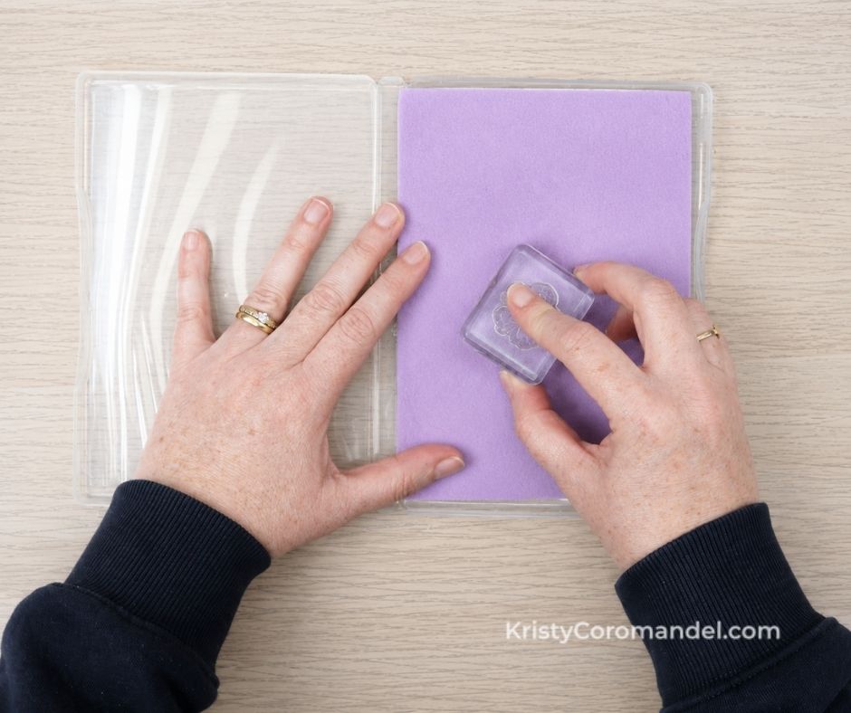 Overhead view of hands gently wiping a clear photopolymer stamp across a damp Simply Shammy inside a clear stamp case to remove ink after stamping.