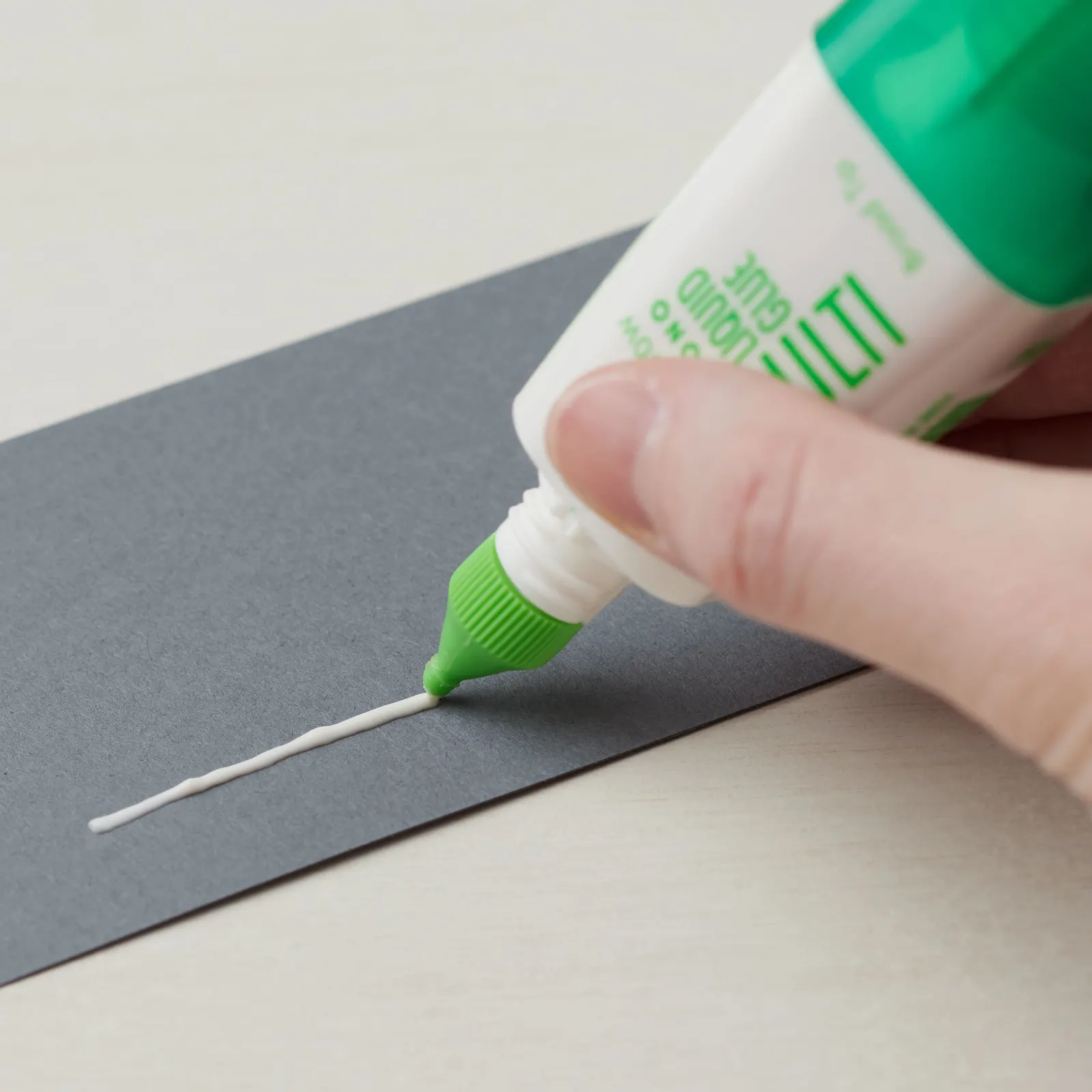 Applying a thin line of liquid glue to cardstock for cardmaking